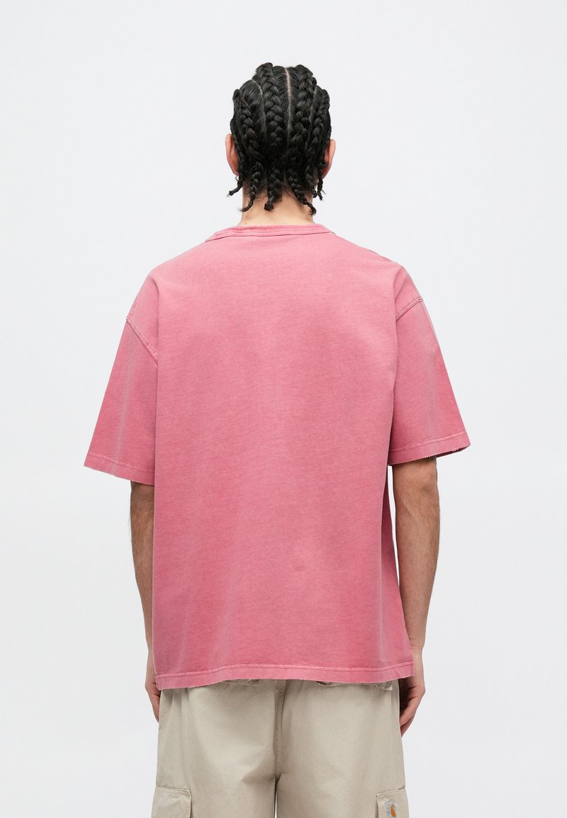 Lyserød, oversized T-shirt med korte ærmer og rund hals. Stoffet virker blødt med en diskret tekstur og afslappet pasform.