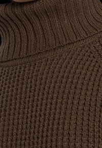 Brauner, gestrickter Rollkragenpullover mit strukturiertem Rippenmuster, ausgestattet mit einem hohen Kragen und einem kreisförmigen Webmuster über den gesamten Körper.