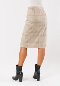 Gonna a matita a quadri beige con un design aderente, vita alta e un'etichetta sul retro; abbinata a stivaletti neri con tacco.