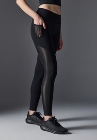 Black athletic leggings with a high waistband, featuring mesh panels on the sides and a side pocket. Smooth texture, fitted design.