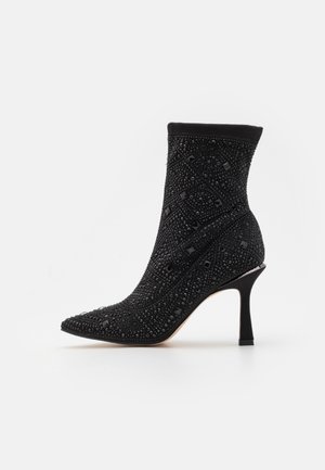 Bottine noire en tissu texturé avec ornements incrustés, bout pointu et talon fin incurvé. Offre un ajustement près du pied.