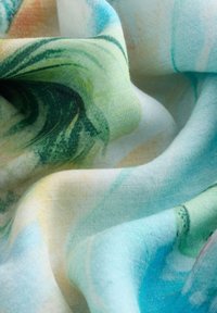 Tissu doux avec des motifs abstraits verts, bleus et beiges semblables à une aquarelle, montrant des plis et une texture en gros plan.