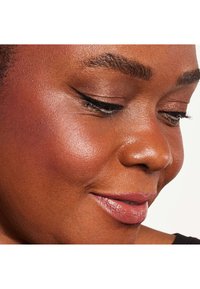 Primo piano di un volto con pelle liscia e tonificata, leggero fard, sopracciglia ben definite e eyeliner applicato con maestria; labbra in una delicata tonalità nude.