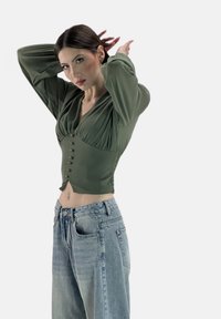 Olivgrünes, bauchfreies Top mit Knopfleiste und plissierten Details, kombiniert mit hellblauen, locker sitzenden Jeans mit hoher Taille.