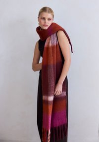 Wollen sjaal met horizontale strepen in tinten rood, roze en oranje, met franjes aan de uiteinden, draped om de nek.