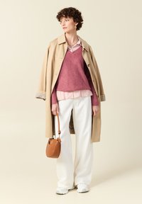 Beżowy trencz, oversize różowy sweter, białe spodnie z szerokimi nogawkami i brązowa torebka. Teksturowe warstwy z paskowanym wzorem i casualowe sneakersy.