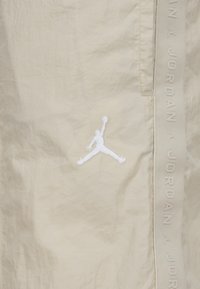 Bež sportske kratke hlače sa istaknutim bijelim izvezenim Jumpman logotipom sprijeda i strukturiranim pojasom s natpisom "JORDAN".