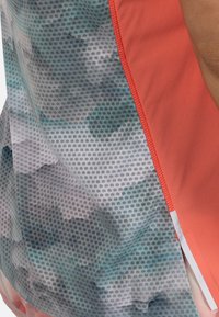 Coral athletic top featuring a patterned mesh side panel with shades of blue and gray, detailed stitching along the edges.