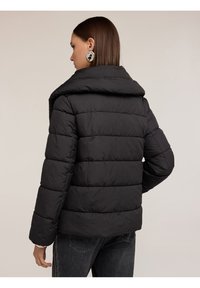 Giacca a vento nera con ampio colletto e design trapuntato. Presenta una vestibilità rilassata e maniche lunghe. La texture sembra morbida e imbottita.