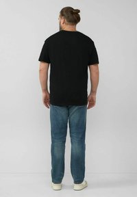 Schwarzes Baumwoll-T-Shirt mit lockerer Passform und rundem Halsausschnitt. Getragen mit leicht taillierten blauen Jeans und weißen Sneakern.