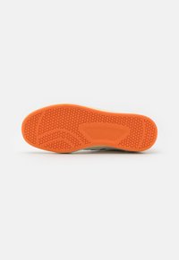 Semelle de chaussure en caoutchouc orange avec une texture en nid d'abeille. Présente un bord lisse et arrondi ainsi qu'une semelle intermédiaire blanche contrastante.