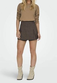 Brązowy sweter prążkowany zestawiony z brązową kraciastą mini spódnicą z fałdami. Noszony z kremowymi kowbojkami z ozdobnym przeszyciem.