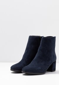 Bottines en daim bleu marine à talon bloc, dotées d'une texture lisse et d'une fermeture éclair latérale pour un enfilage facile. Forme à bout arrondi.