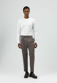 Witte blouse met lange mouwen en grijze gestreepte broek met geplooide voorkant en riemlusdetail, gecombineerd met donkerbruine loafers.