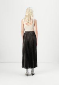 Jupe maxi plissée noire avec une texture lisse et une large taille, associée à un débardeur ajusté crème et des chaussures à talons grises.