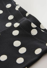 Tissu noir à pois blancs, présentant une texture côtelée. Vue en gros plan mettant en évidence les détails et les coutures du tissu.