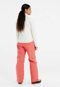 Top grigio chiaro a maniche lunghe con colletto alto e dettagli rosa, abbinato a pantaloni rosa corallo. Entrambi sono realizzati in materiali morbidi e flessibili.