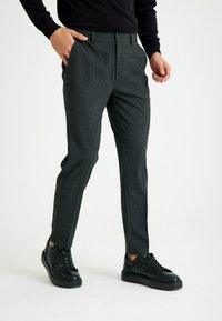Grijze geruite broek met een op maat gemaakte pasvorm, platte voorkant en zijzakken, gecombineerd met zwarte sneakers. Gladde textuur en subtiele patroondetails.