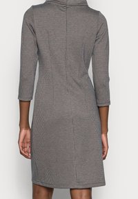 Šedé kostkované šaty s dobře padnoucím střihem, tříčtvrtečními rukávy a vysokým výstřihem. Tkanina má jemnou strukturu a tvarované švy.