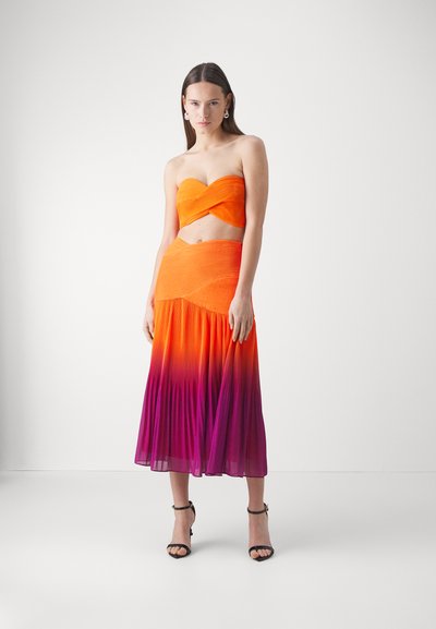 Bežkrūšu bandeau tops spilgti oranžā krāsā ar krokotu dizainu, apvienots ar garu svārku, kuram ir ombre gradienta pāreja no oranžā līdz purpura krāsai.