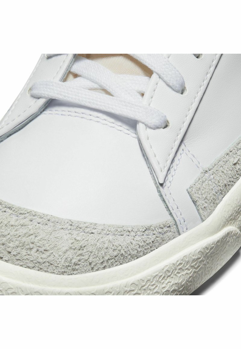 Sneaker bianco con punta in suede grigio texture, parte superiore in pelle bianca liscia, lacci bianchi e suola in gomma con motivo.