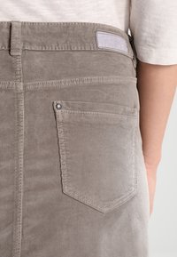 Grauer Cordrock mit strukturierter Oberfläche, ausgestattet mit einer Gesäßtasche, die einen sichtbaren Metallnieten und Nahtdetails aufweist.