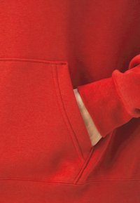 Main partiellement dans la poche avant d'un sweat-shirt rouge vif avec un poignet côtelé sur la manche.