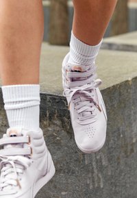 Vita högskor med ljuslila detaljer, texturerat läder, perforerad tå och snörningsdesign, tillsammans med vita ribbade strumpor.