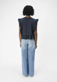 Haut sans manches bleu marine avec des volants aux épaules et un motif texturé, associé à un jean large taille haute bleu clair.