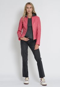 Lyserød læderjakke med grå hætte, tætsiddende design, lynlås i front og ribbede detaljer. Bæres med grå top og sorte jeans.