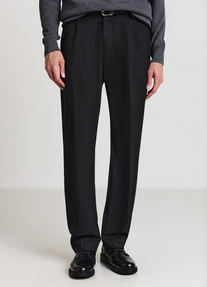 Schwarze, maßgeschneiderte Hose mit glatter Textur, versehen mit Falten und geradem Bein, kombiniert mit schwarzen Lederschuhen.