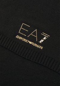 Svart strikket stoff med ribbet kant. Gyllen pynt danner teksten "EA7" og "Emporio Armani" med en subtil glitrende effekt.