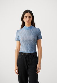 Ljusblå, kortärmad topp med hög hals, med ett texturerat rutmönster och varumärkeslogotyp, parat med höga svarta jeans.