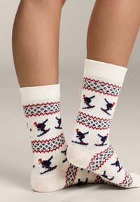 Kremaste pletene čarape s uzorkom koji uključuje crvene i mornarsko plave naglaske, uključujući stilizirane ptice i geometrijske oblike.