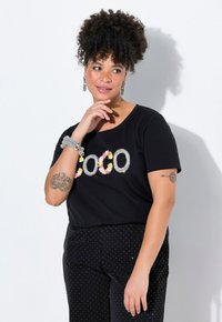 Camiseta negra de manga corta con el texto "COCO" en un diseño floral y de strass, combinada con pantalones negros de lunares.