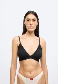 Bezprzewodowy czarny biustonosz typu braletka z dekoltem w kształcie litery V, panelami z siateczki i regulowanymi ramiączkami. Gładka faktura i minimalistyczny styl.