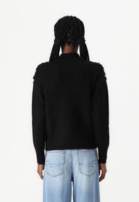 Maglione nero con colletto alto, dettagli testurizzati sulle spalle e maniche lunghe, abbinato a pantaloni a gamba larga blu chiaro.
