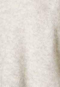 Gaiši pienbaltas vilnas džemperis ar mīkstu, fakturētu adījumu un smalkām krāsas variācijām, izceļot mājīgu un siltu izskatu.