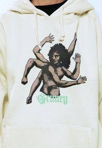 Sudadera crema con un gráfico de una figura con múltiples brazos. El diseño está impreso en negro y verde, con un acabado texturizado.