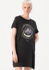 Svart t-shirt klänning i mjuk bomull med en lotusgrafik som har geometriska inslag i lila och guld, samt en avslappnad passform.