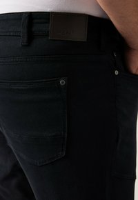 Jeans in denim nero con una texture liscia, dotati di un'etichetta in pelle MEN+ in vita e bottoni in metallo sulle tasche.