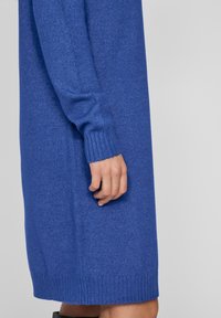 Blå stickad klänning med långa ärmar, ribbad mudd och nederkant. Mjuk textur med rak passform som når mid-lår.