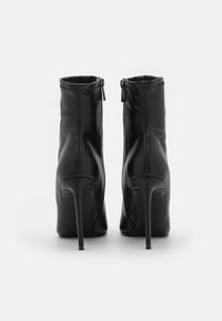 Zwarte hoge enkellaarsjes, gemaakt van soepel leer, hebben een taperend design met ritssluiting en spitse stilettohakken.