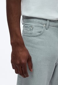 Svetlosivé rifle z denimu s textúrovaným povrchom, s klasickým strihom, prednými vreckami a malou značkovou nálepkou na zadnom vrecku.