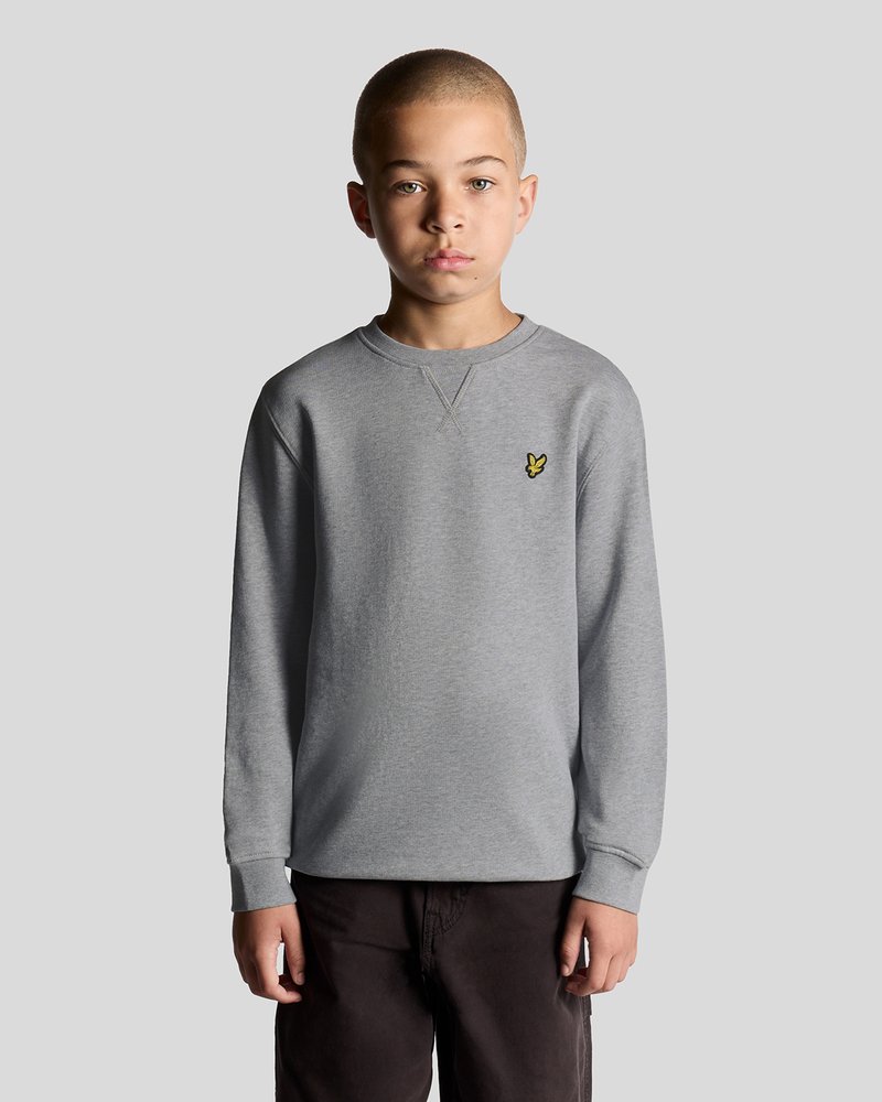 Sweatshirt gris à manches longues avec un col rond et des poignets côtelés, arborant un petit logo jaune sur la zone gauche de la poitrine.