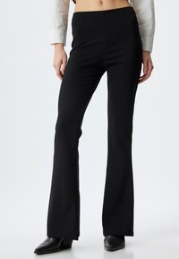 Pantalones negros acampanados hechos de tela elástica, con una cintura alta y una textura suave, combinados con zapatos negros de punta.