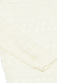 Gräddfärgad stickad tyg med ett strukturerat mönster av små utskurna prickar och ribbade ärmslut. Mjuk, andningsbar och lätt material.