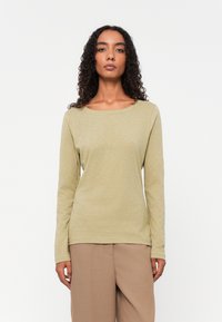Langermet skjorte i lys olivengrønn, laget av mykt stoff, med rund hals og en avslappet passform, iført med beige bukser.