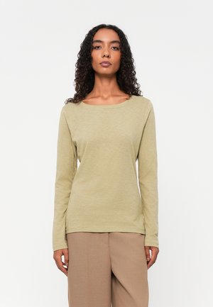 Langermet skjorte i lys olivengrønn, laget av mykt stoff, med rund hals og en avslappet passform, iført med beige bukser.