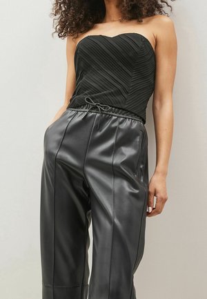 Woman wearing black strapless textured top and high-waisted black faux leather pants with drawstring waist and front pockets.